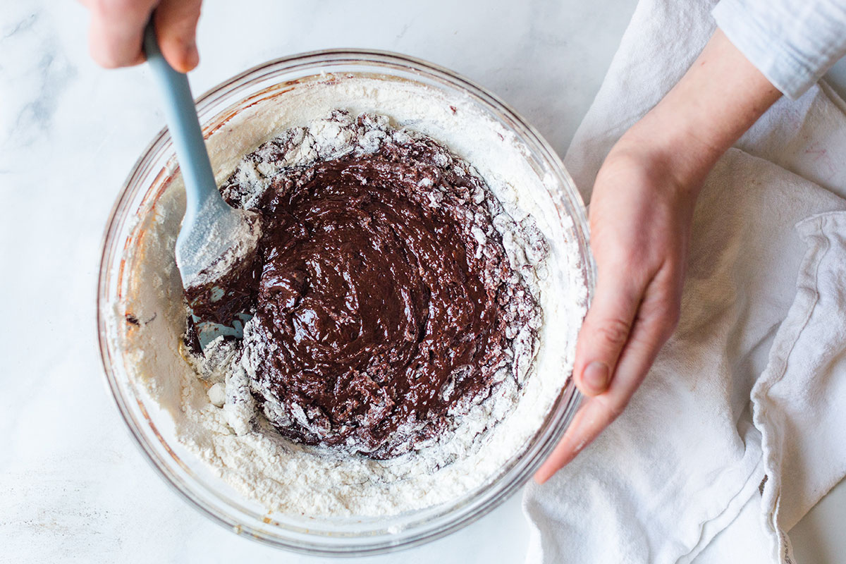 A baker mixing the dry ingredients into melted chocolate and butter to make Chocolate Crinkles
