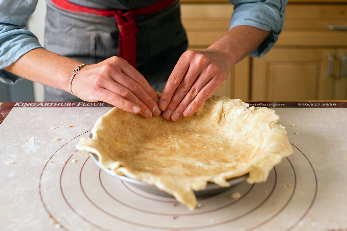 A baker shaping the bottom crust for a cinnamon bun apple pie into a pan