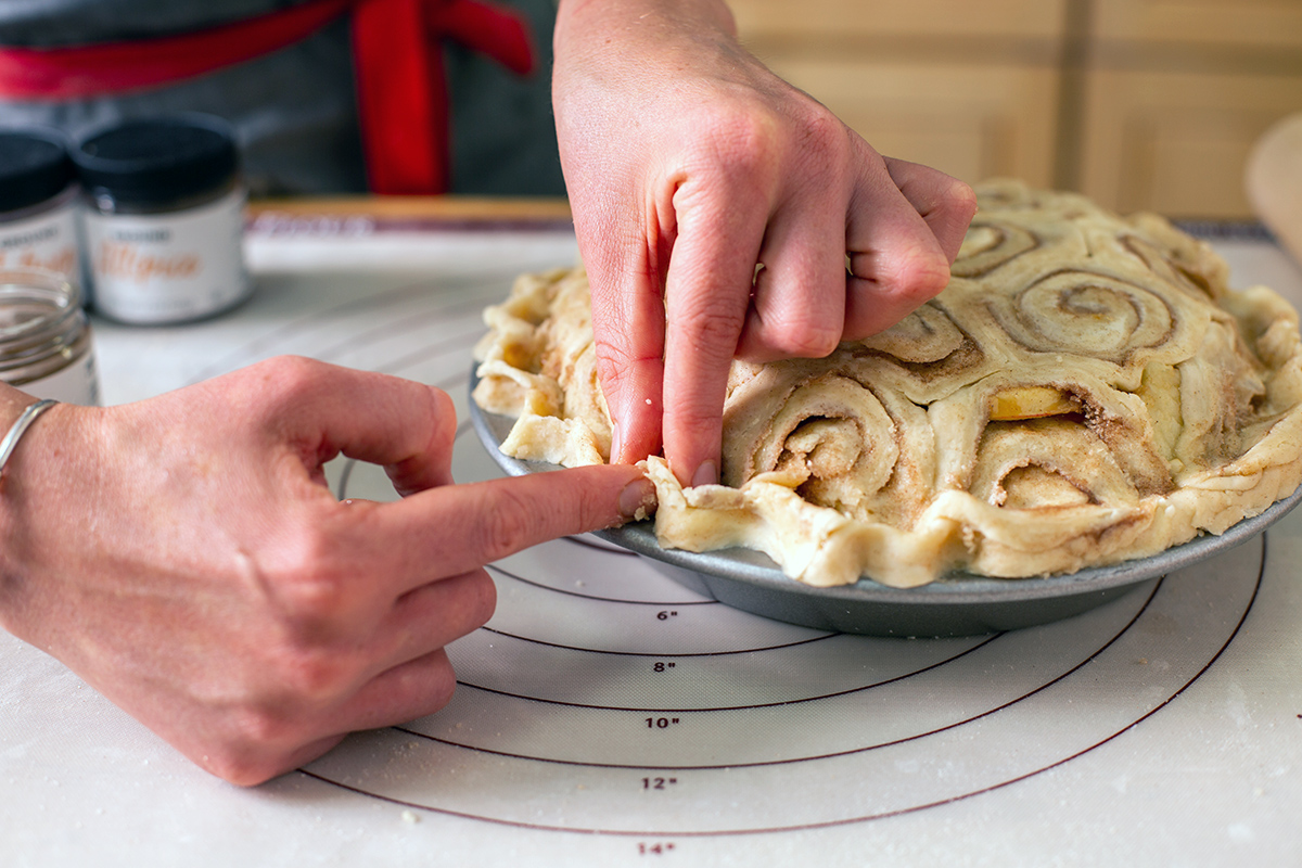 A baker arranging a cinnamon bun crust on top of an apple pie