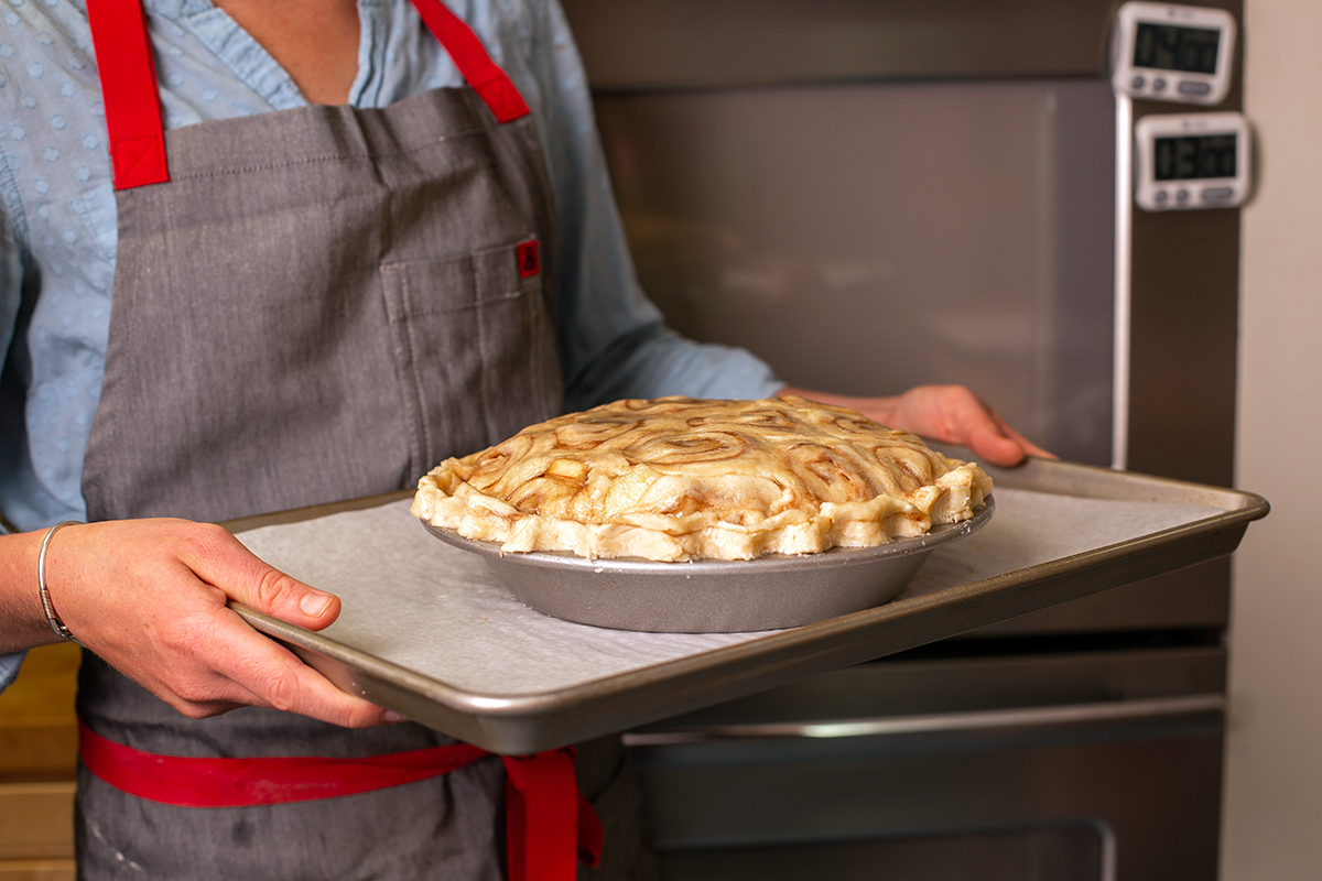 A baker holding an unbaked cinnamon bun apple pie, ready to go in the oven