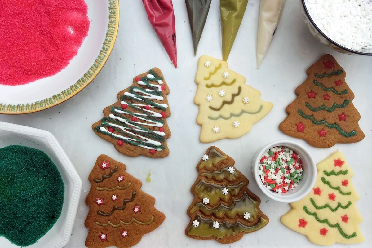Bowls of natural sprinkles and bags of icing next to Christmas tree-shaped cookies