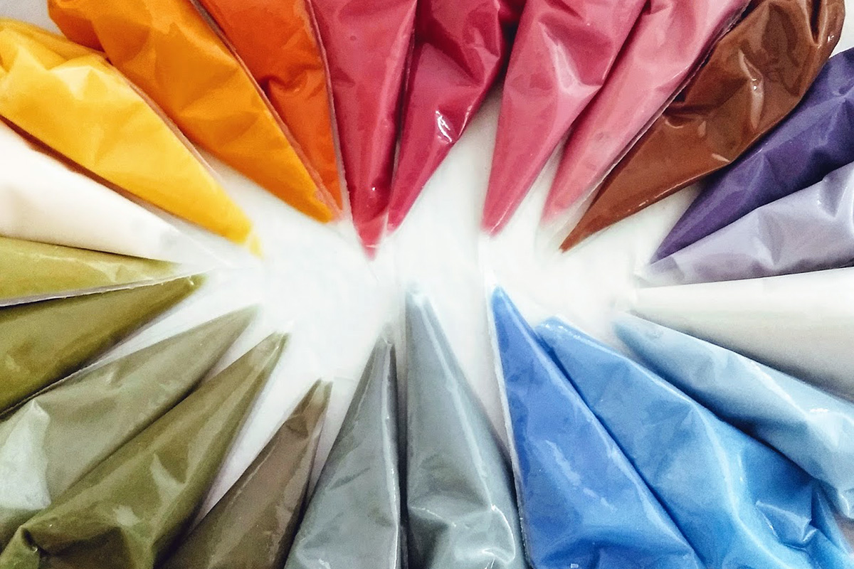 An array of pastry bags filled with naturally-colored icing, all colors of the rainbow