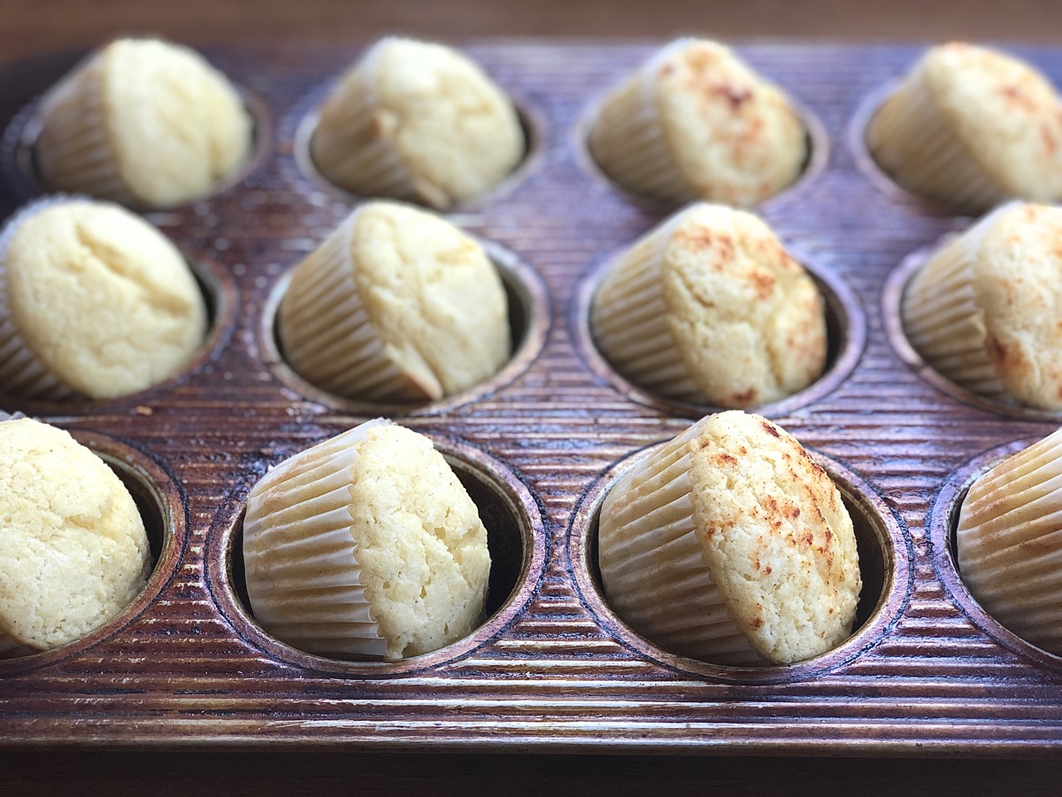 Baked corn muffins tilted in the wells of a muffin pan cooling off