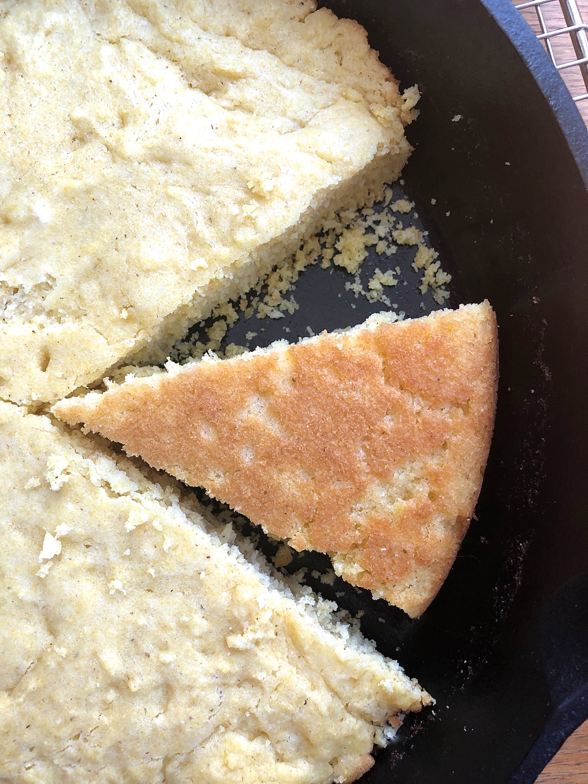 A wedge of baked cornbread turned over in a cast-iron skillet to show its golden brown crust.