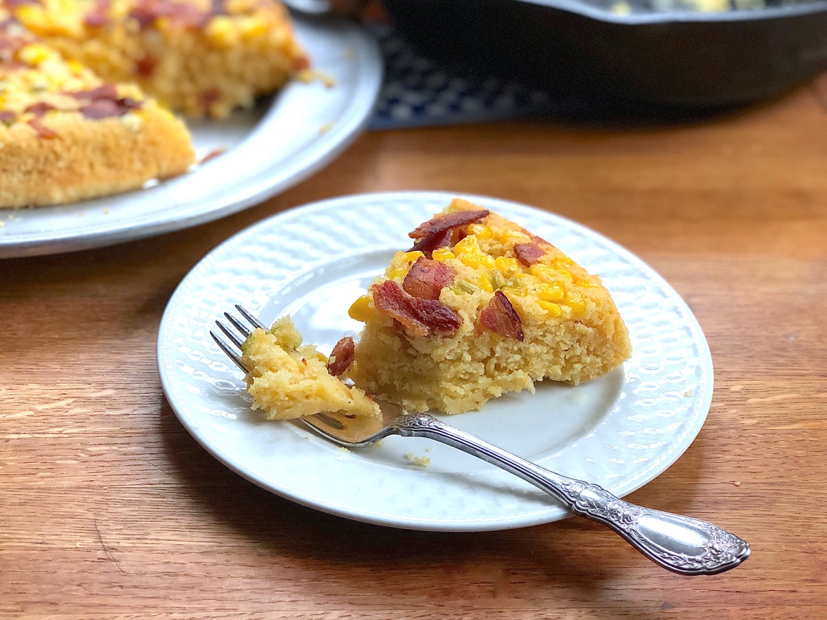 Plated slice of cornbread baked with a topping of scallions, bacon, and corn