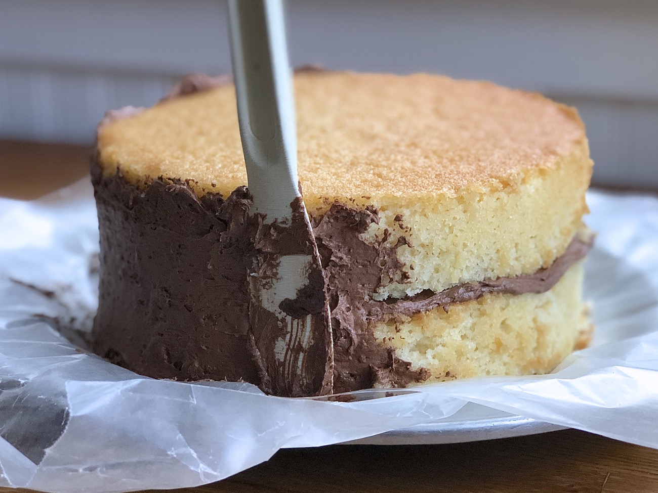Applying a layer of chocolate frosting — the crumb coat  to a double layer yellow cake.