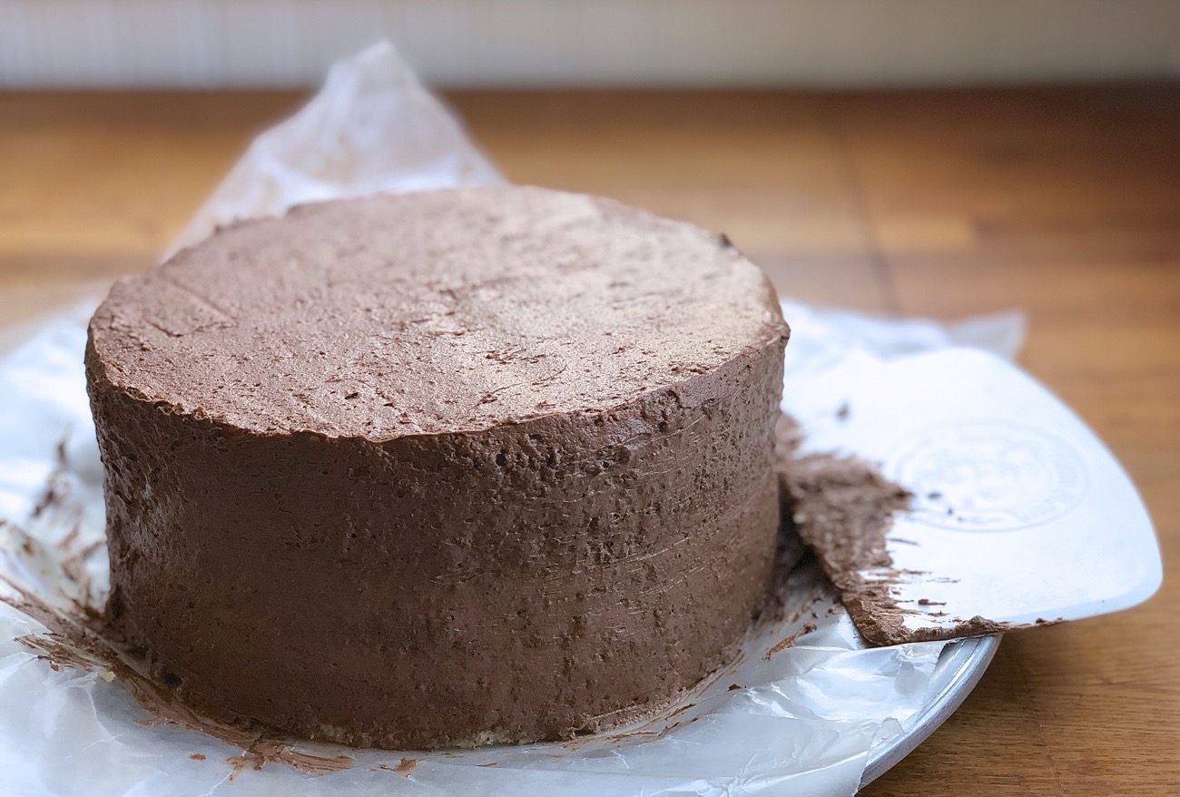A double-layer yellow cake filled and iced with a thin layer of chocolate frosting known as a crumb coat.