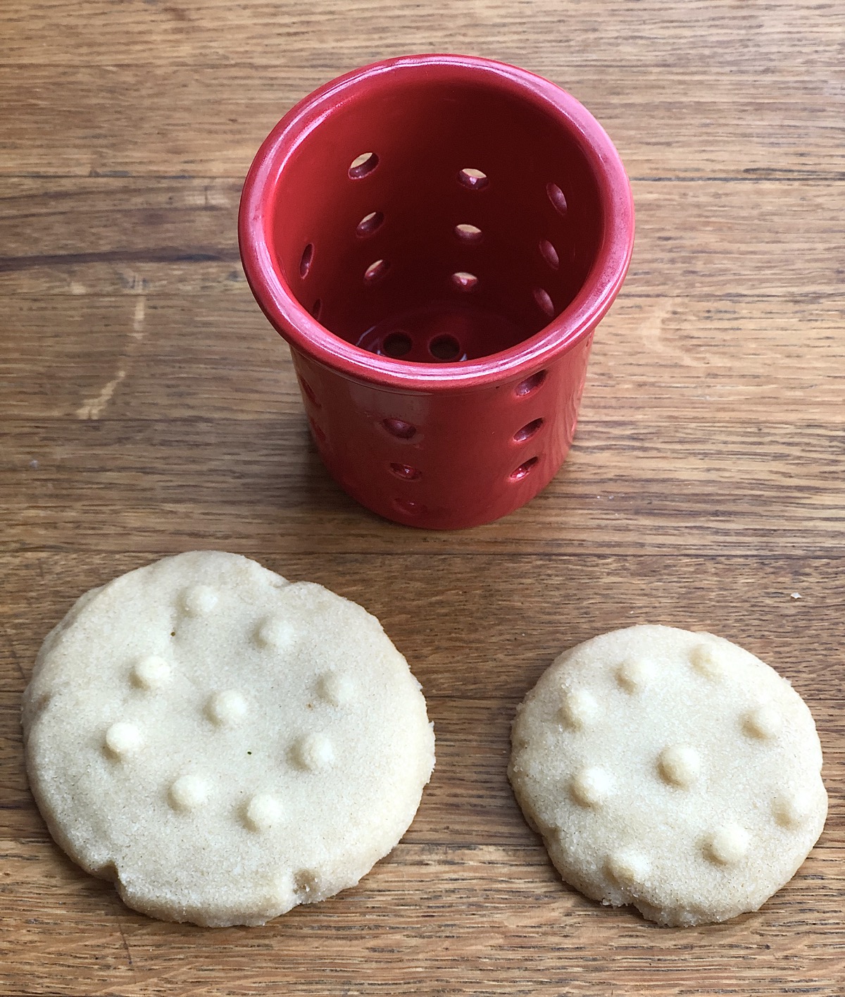 Two chocolate cookies on a table, one large, one small, showing how the imprint made with a tea strainer covers the small cookie, but only partially covers the large one.