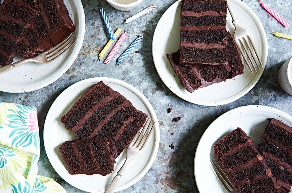 Four-layer fudge cake with chocolate frosting, sliced on a plate.