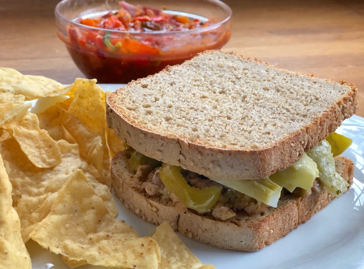 Sandwich made with sourdough sandwich bread on a plate, chips and salsa on the side.