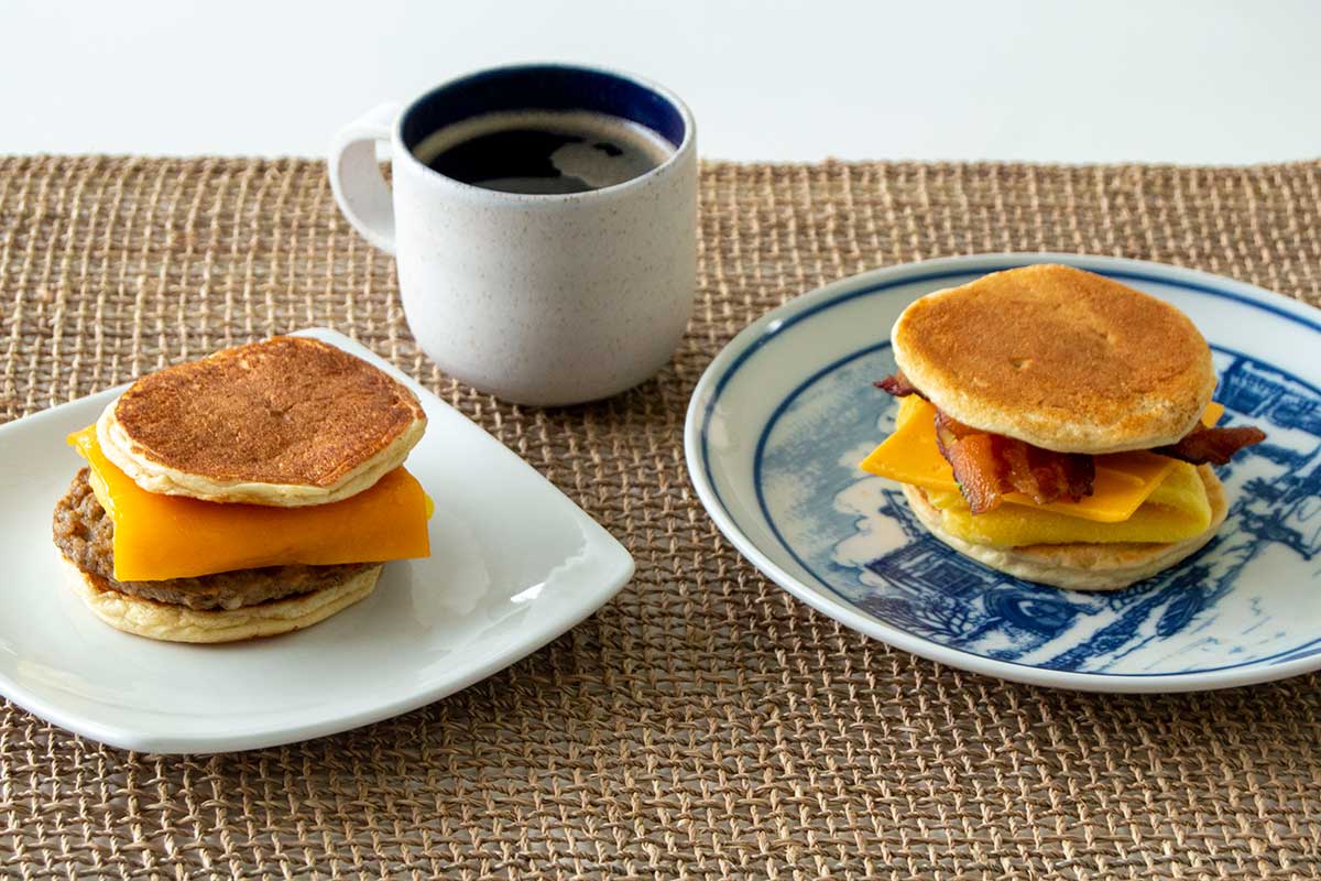 Two breakfast sandwiches made with pancakes as bread -- one with sausage, the other with bacon