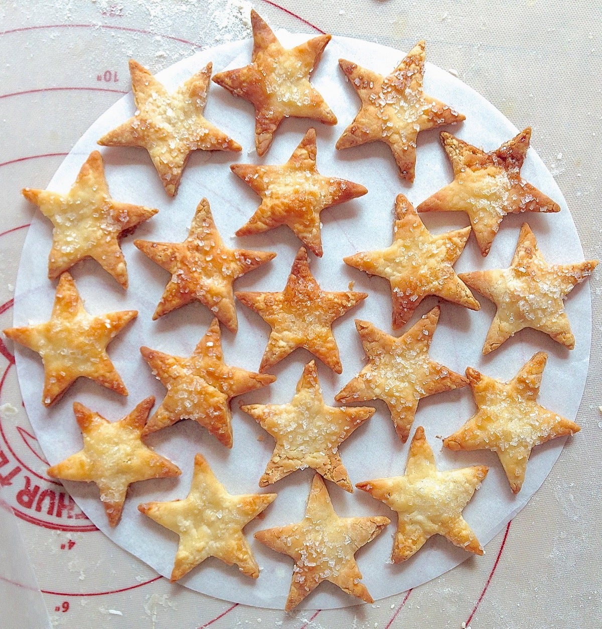 Baked pastry star cutouts arranged on a 9" parchment round to check the design before transferring to the top of a blueberry pie.