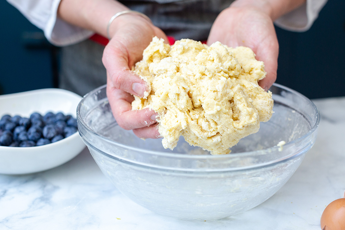 A baker's hands holding out scone dough to show the sticky, craggly texture
