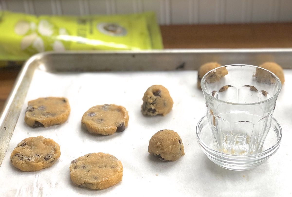 Dough for Gluten-Free Almond Flour Chocolate Chip Cookies flattened on a  baking sheet using the bottom of a drinking glass.