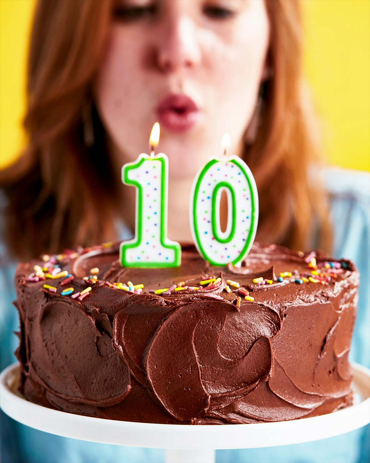 A woman blowing out the candles on a birthday cake with the number 10 on it