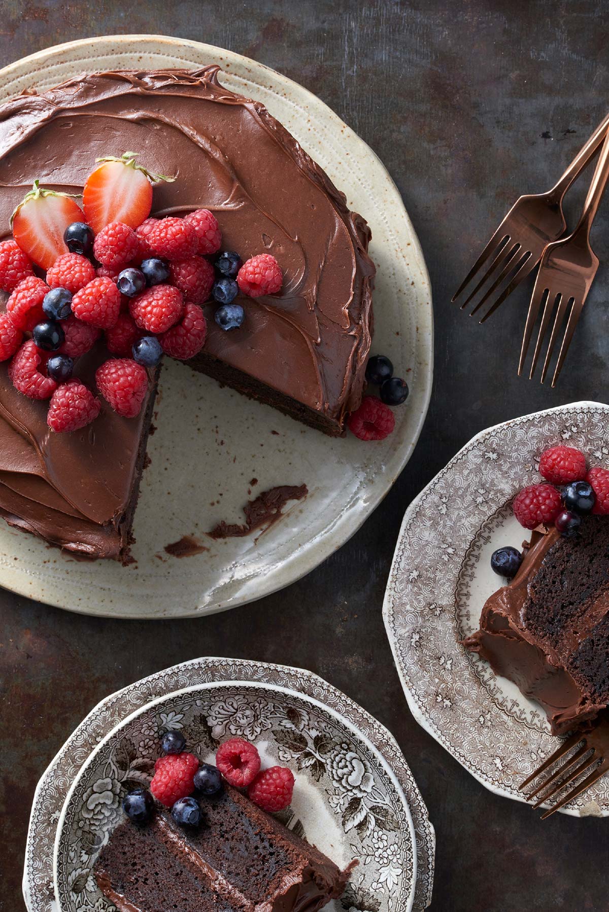 A gluten-free chocolate cake topped with chocolate frosting and fresh fruit with a few slices on plates