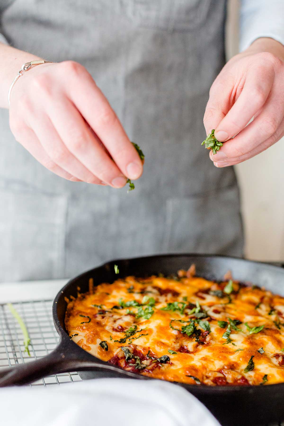 A baker sprinkling fresh herbs on top of a gluten-free pan pizza baked in a cast iron pan