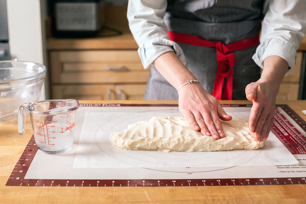A baker patting out gluten-free cinnamon roll dough into an 8" x 16" rectangle