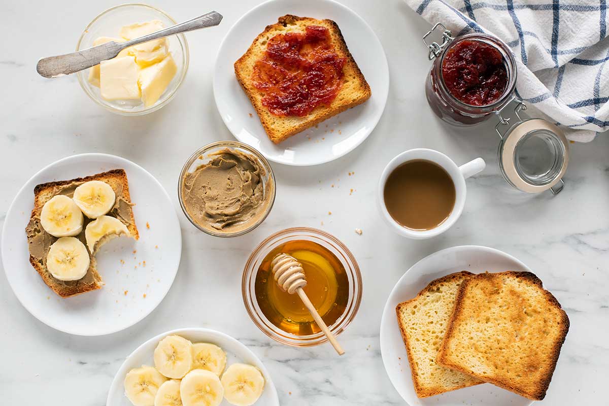 A kitchen table set for breakfast with gluten-free toast, honey, bananas, nut butter, and jam