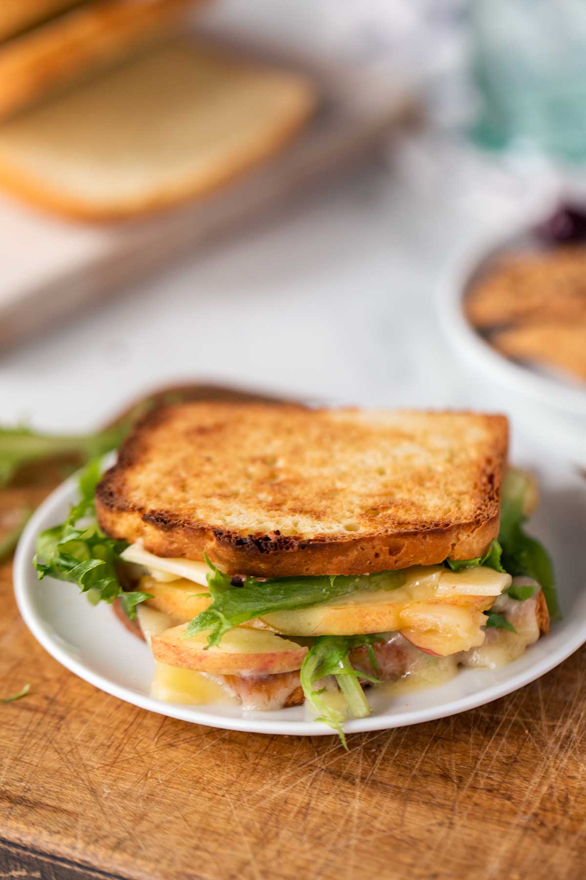 A grilled cheese made with gluten-free bread and garnished with slices of apples and greens