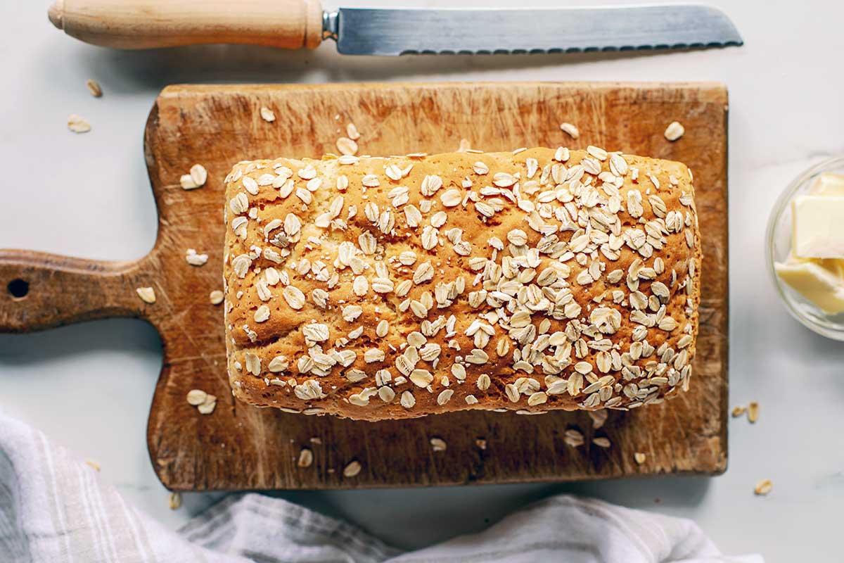 A loaf of gluten-free sandwich bread topped with oats on a bread board