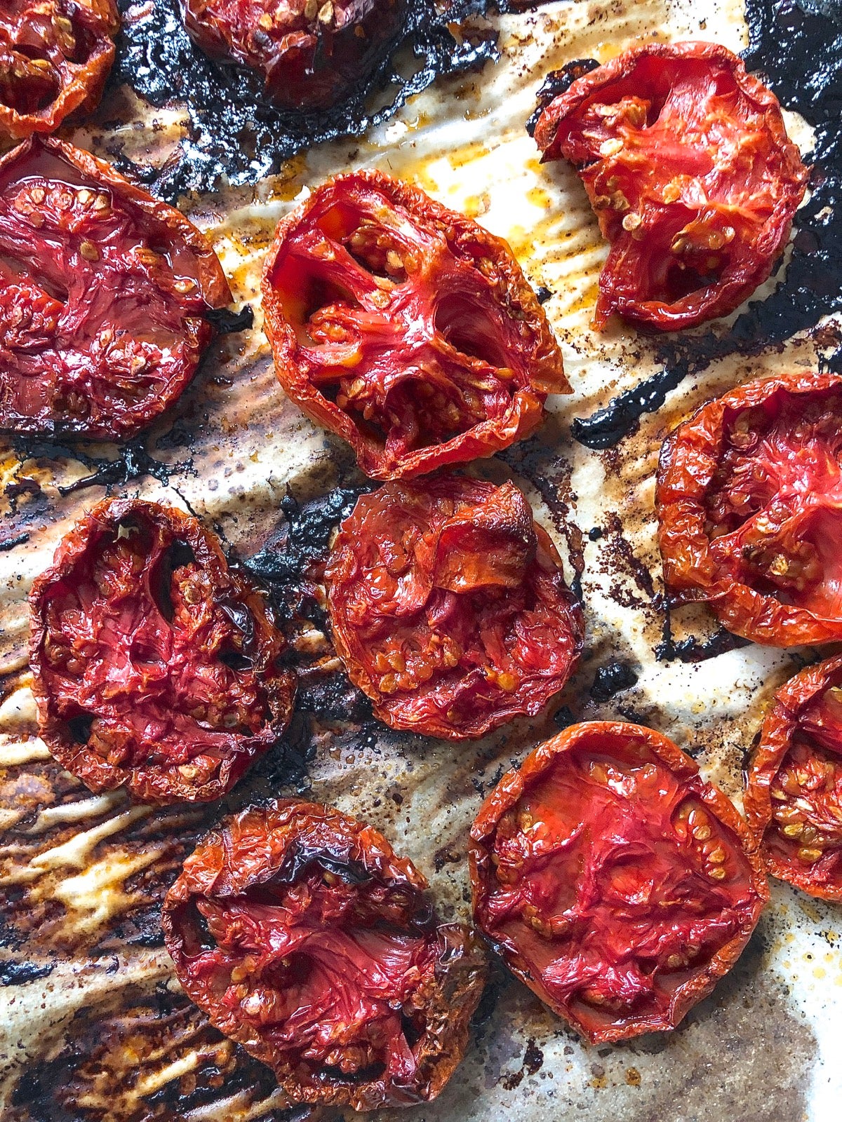 Sliced fresh tomatoes, char-roasted on a parchment-lined baking sheet.