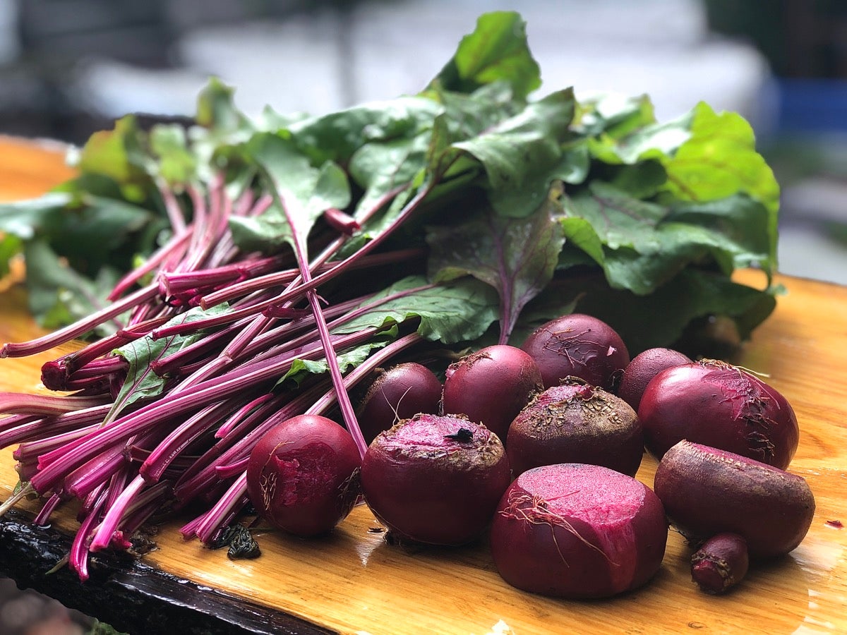 Freshly harvested beets and beet greens on an outdoor cutting board.