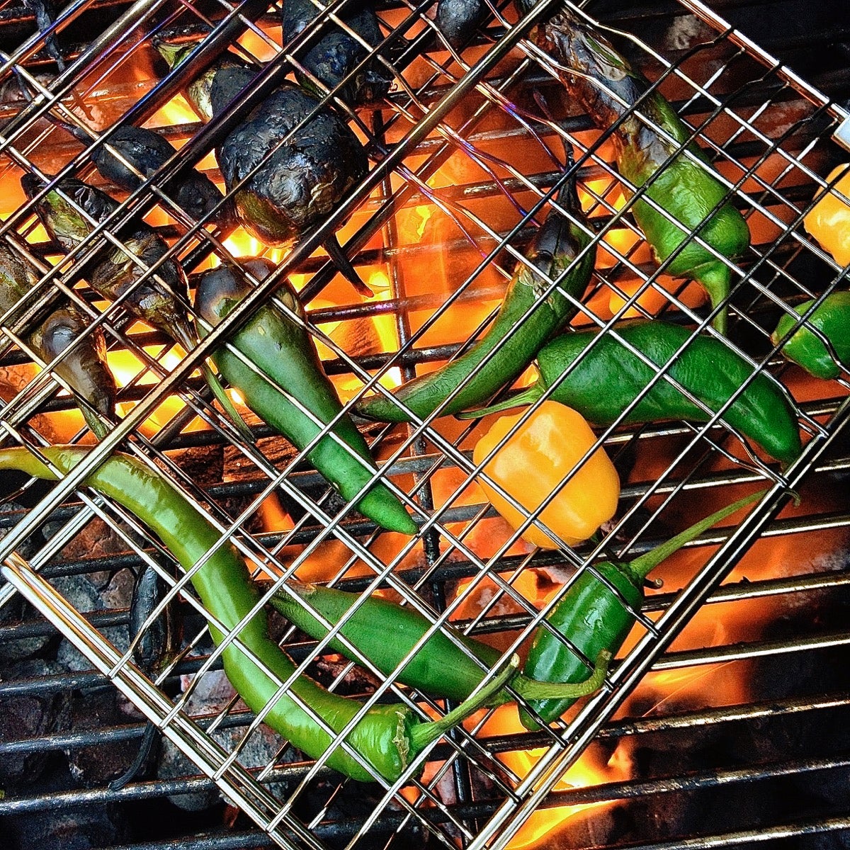 Serrano peppers and small yellow bell peppers charring on an open-flame grill.