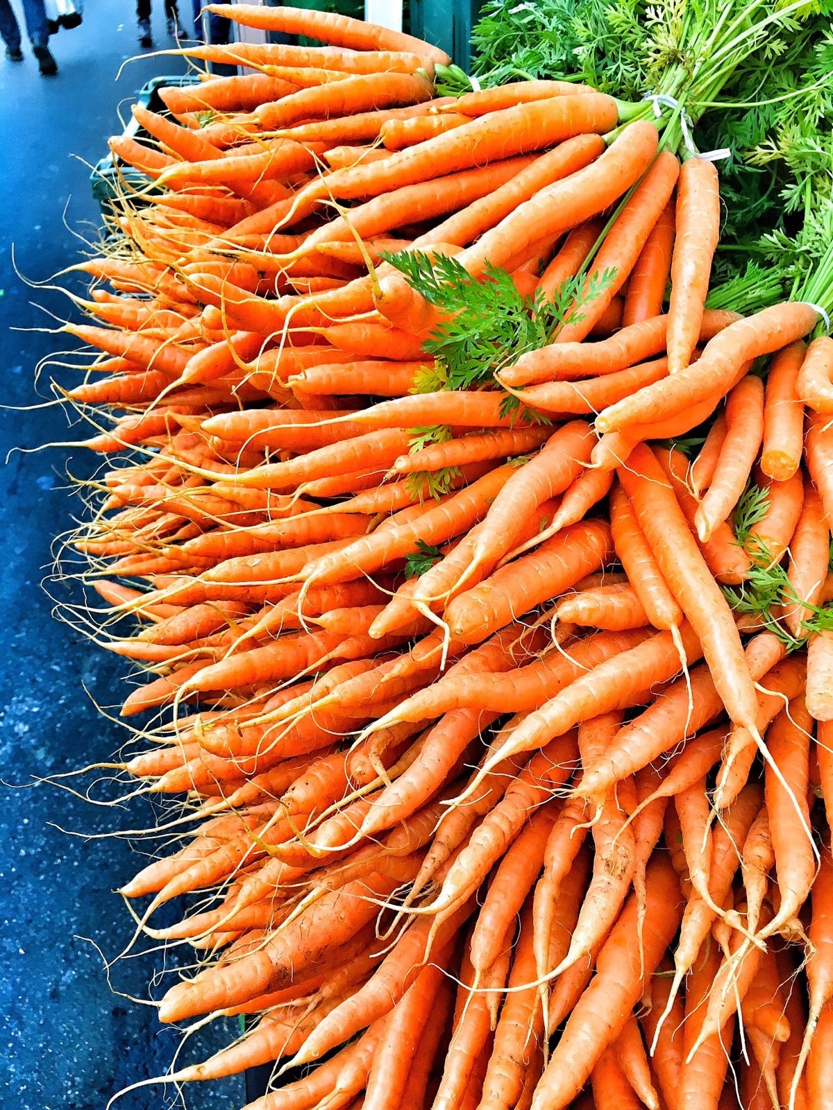 Bunches of thin carrots stacked on a stand at a farmers' market.