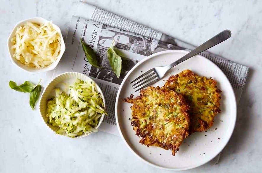 Zucchini pancakes on a plate, with shredded zucchini and grated cheese pictured on the side.