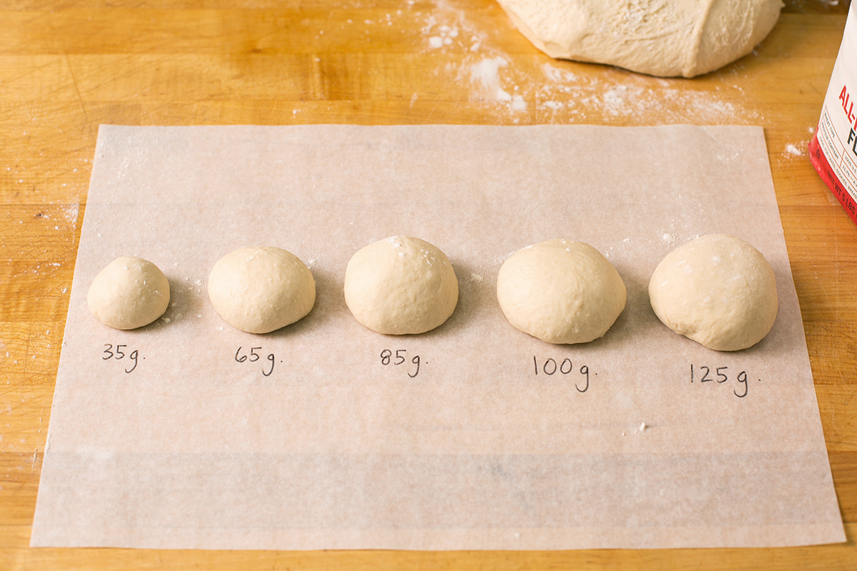 A line up of dough balls of different sizes ranging from 35 grams to 125 grams