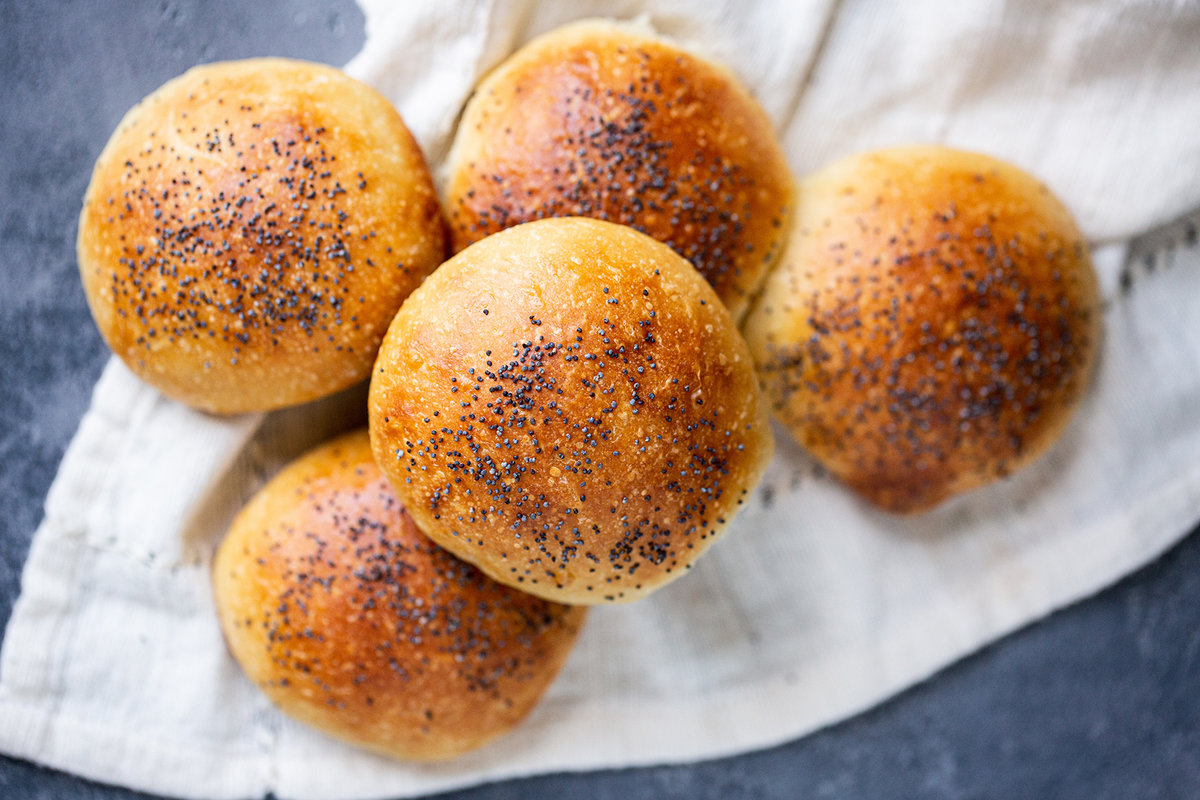 Homemade hamburger buns topped with poppy seeds on a tea towel
