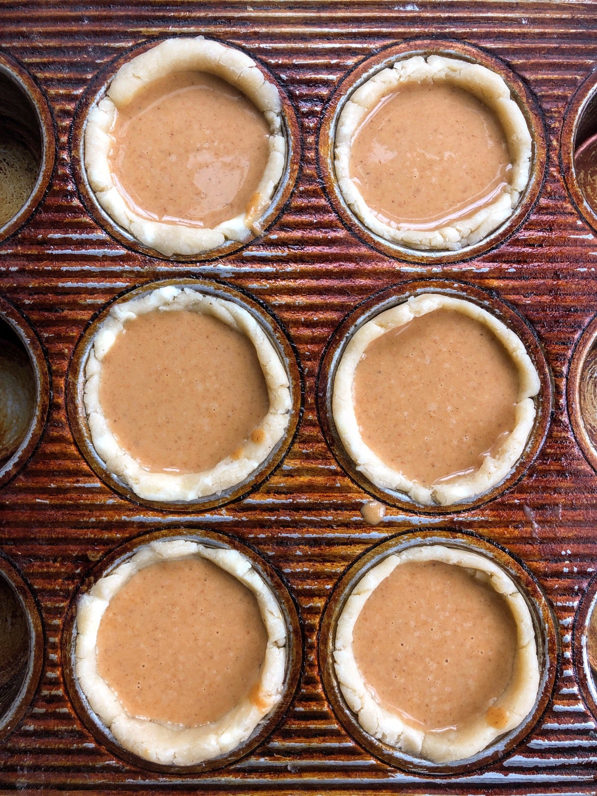 Mini pumpkin pie crusts in a muffin pan, filled and ready to bake.