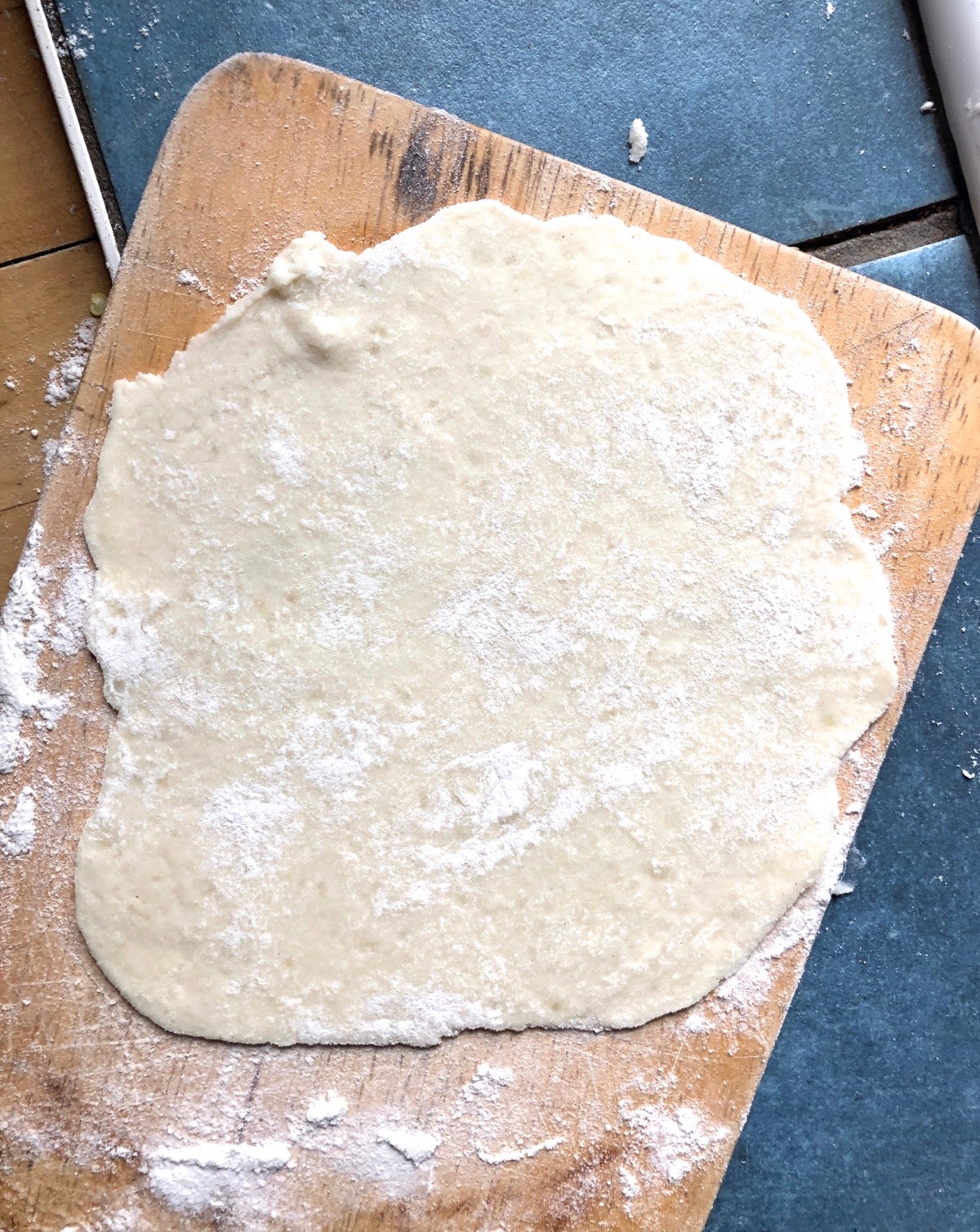 Rolled -out lefse on a floured cutting board, ready to transfer to a frying pan to cook.