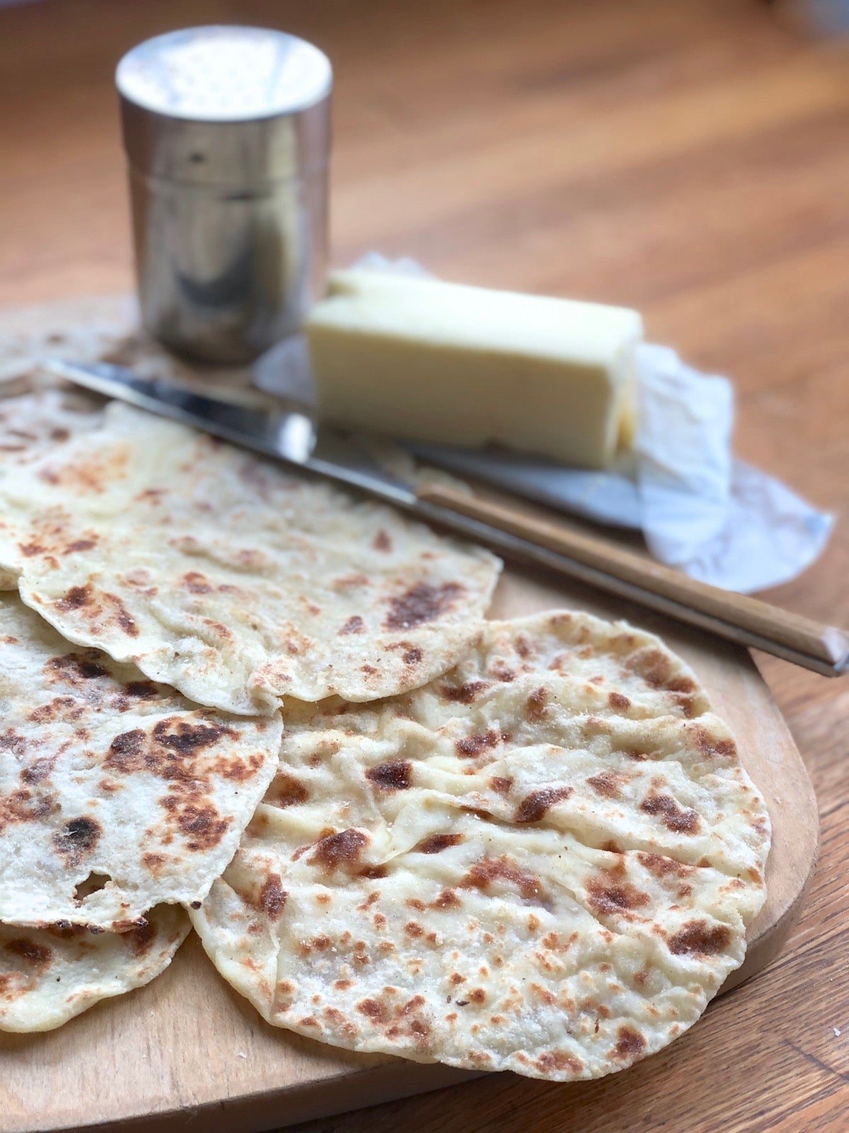 Cooked lefse fanned out on a cutting board, butter and cinnamon sugar in the background.