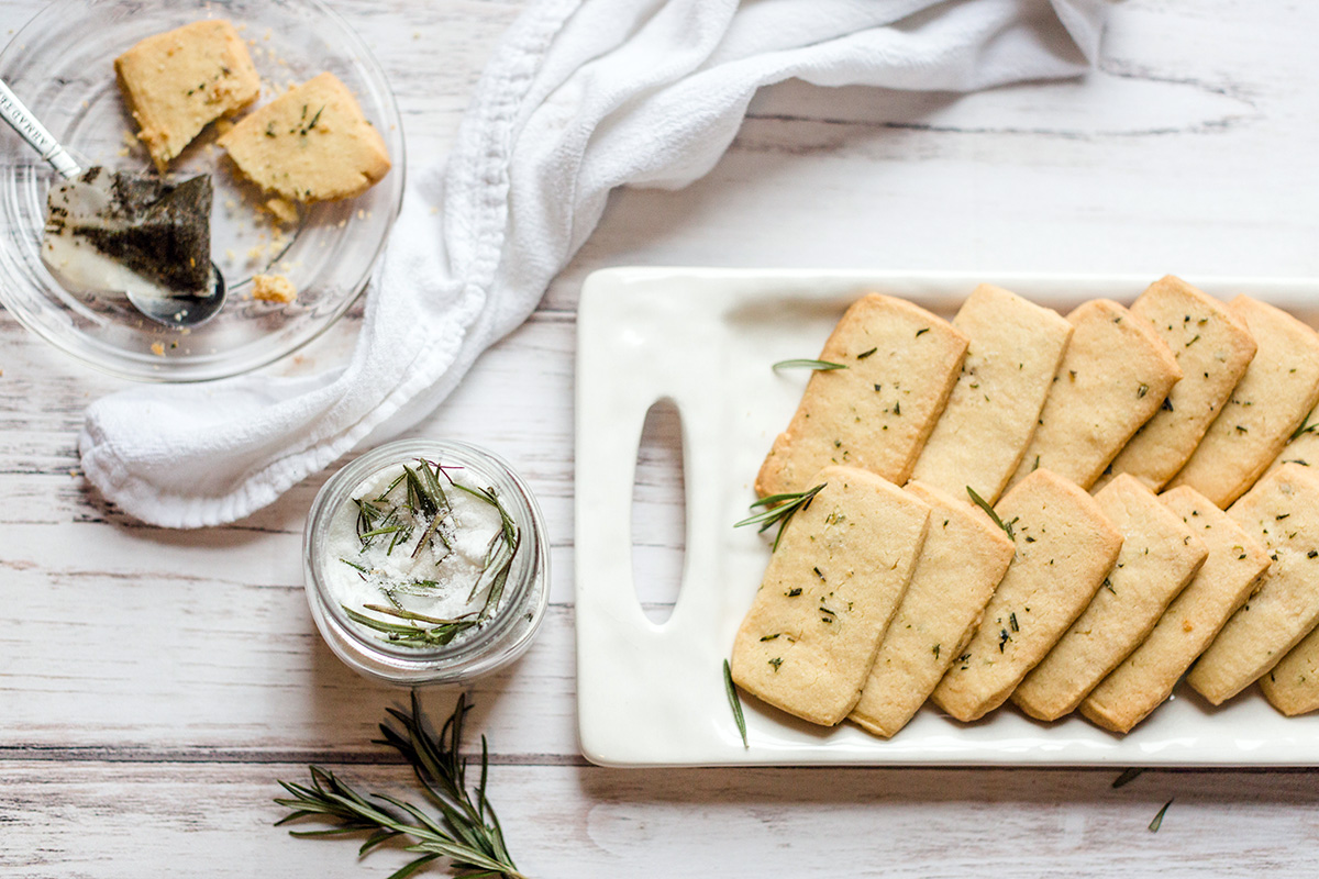 A platter of rosemary shortbread cookies along with a jar of rosemary sugar and a tea bag