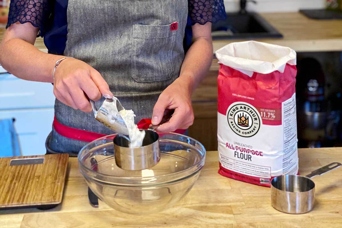 A baker measuring flour into a bowl on a scale