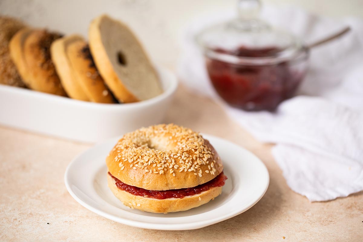 A homemade sesame bagel on a plate with strawberry jam
