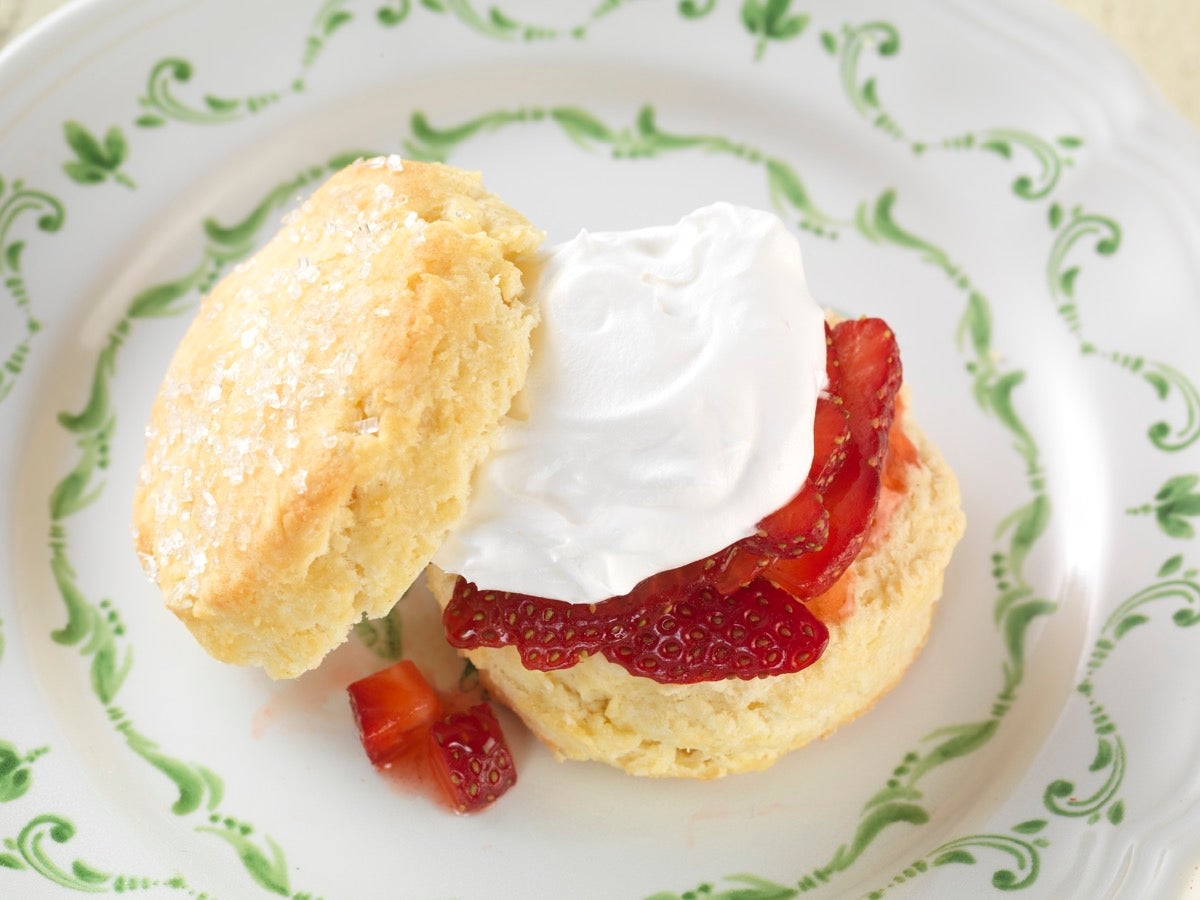 Strawberry shortcake: a biscuit topped with cut berries and whipped cream, all on a saucer.