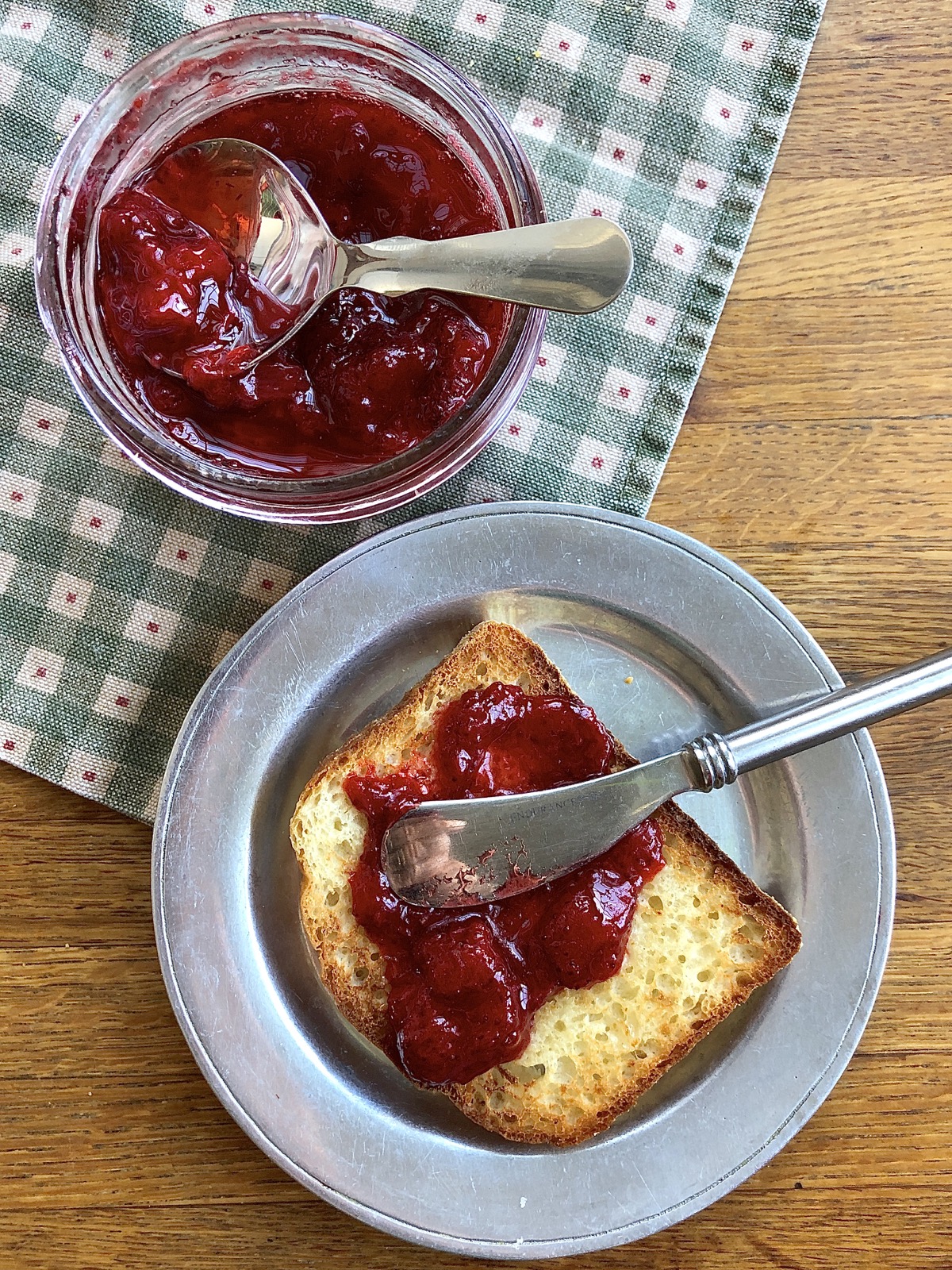 Slice of buttered toast with strawberry jam, jar of jam with spoon.