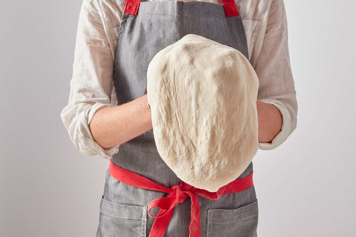 Standing baker shaping dough into a pizza shape 
