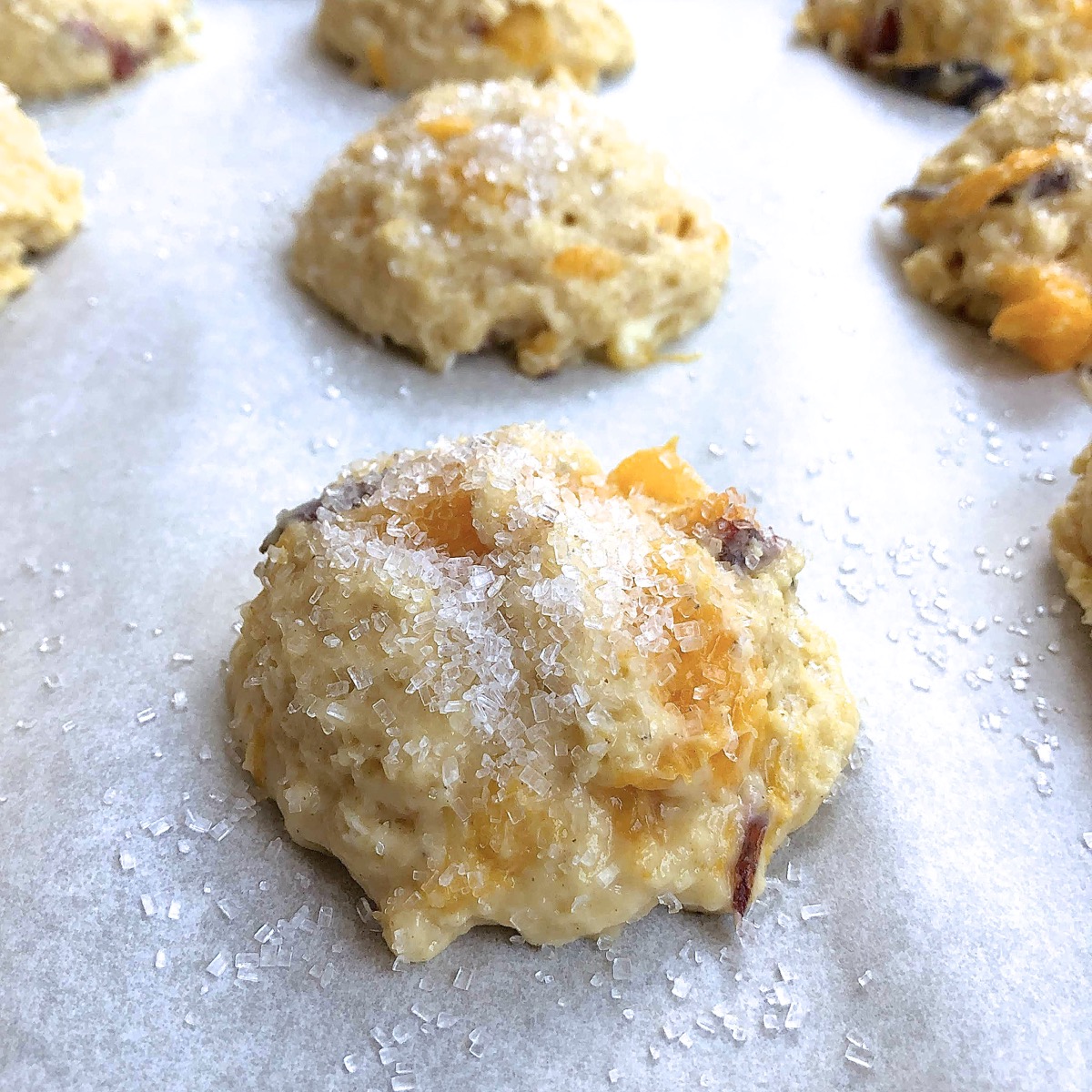 An unbaked peach scone garnished with coarse white sparkling sugar, ready to be baked. 