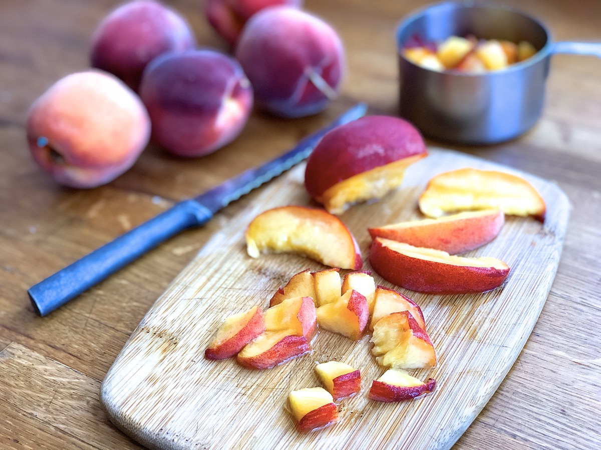 A fresh unpeeled peach cut into slices and then chunks on a cutting board. 