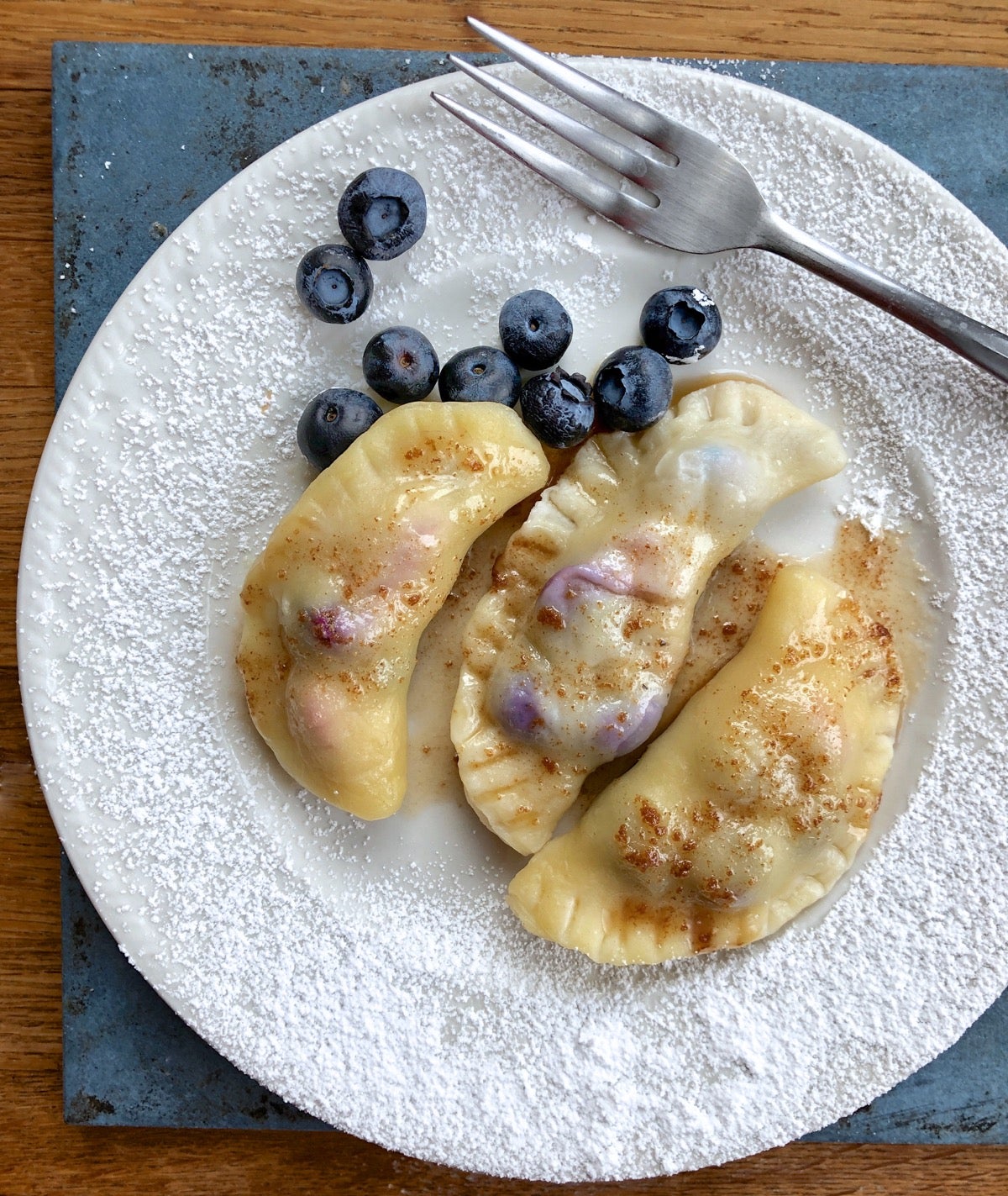 Fresh berry pierogi on a plate, drizzled with brown butter and dusted with confectioners' sugar .