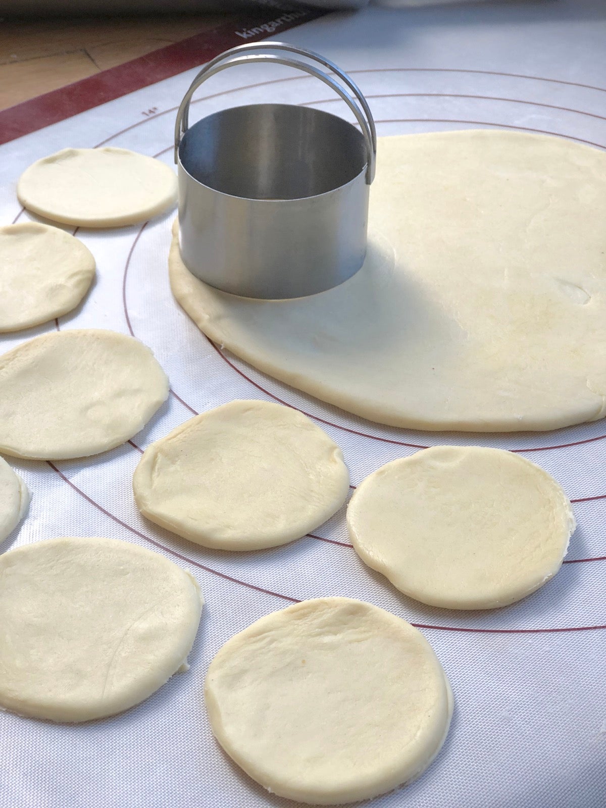 Rolled pierogi dough on a silicone mat being cut with a round biscuit cutter.
