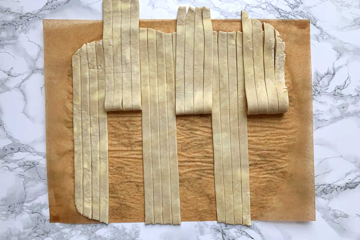 Sheet of dough cut into vertical strips, alternating between four strips pulled back and four laying flat