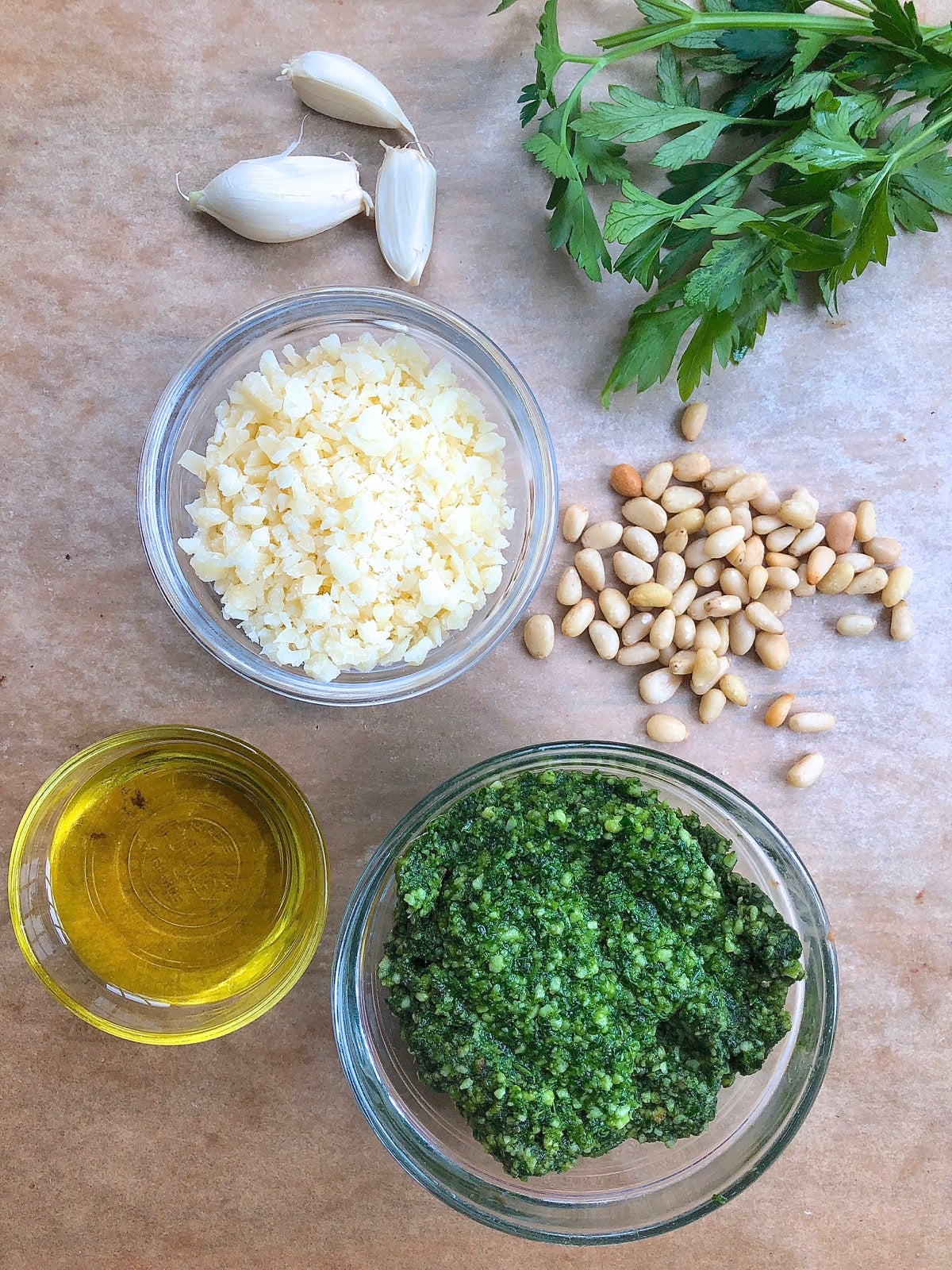 Ingredients for pesto sauce, incouding parsley, grated Parmesan, olive oil, pine  nuts, and garlic cloves