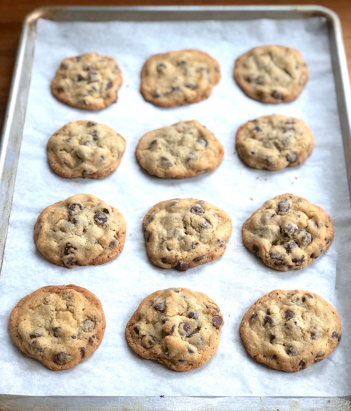 Rows of baked chocolate chip cookies on a parchment-lined baking sheet.