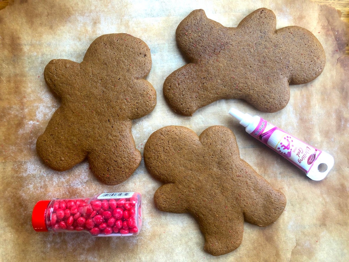 Gingerbread men on a baking sheet, no decorations, flanked with a tube of decorating gel and bottle of candy decos.