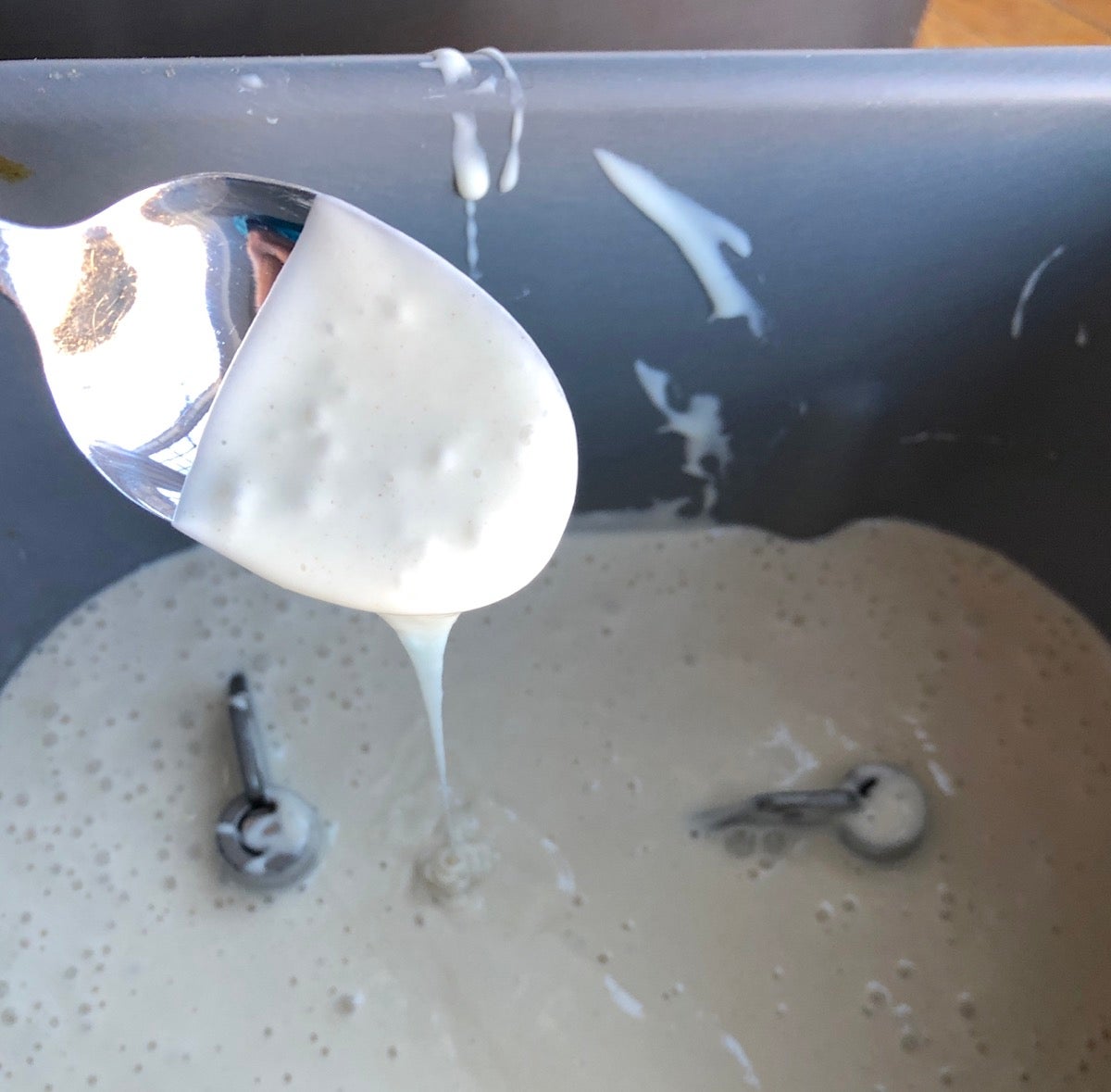 Sourdough starter dripping from a spoon into a bread machine bucket.